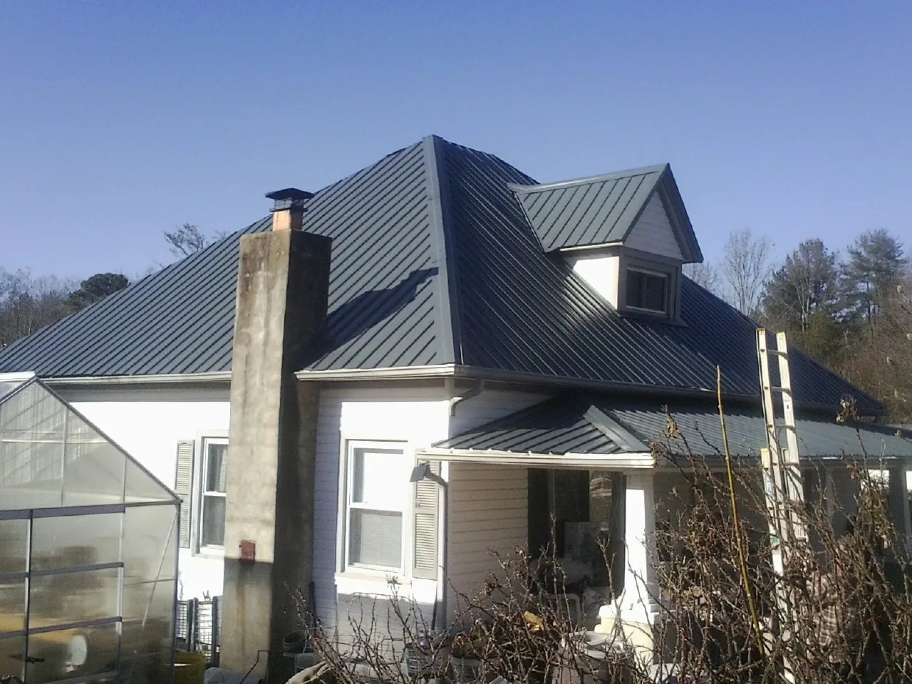 Dark blue standing seam metal roof on a white farmhouse with dormer — Slate & Tile Roof Repair by Roofing Brothers in Saegertown