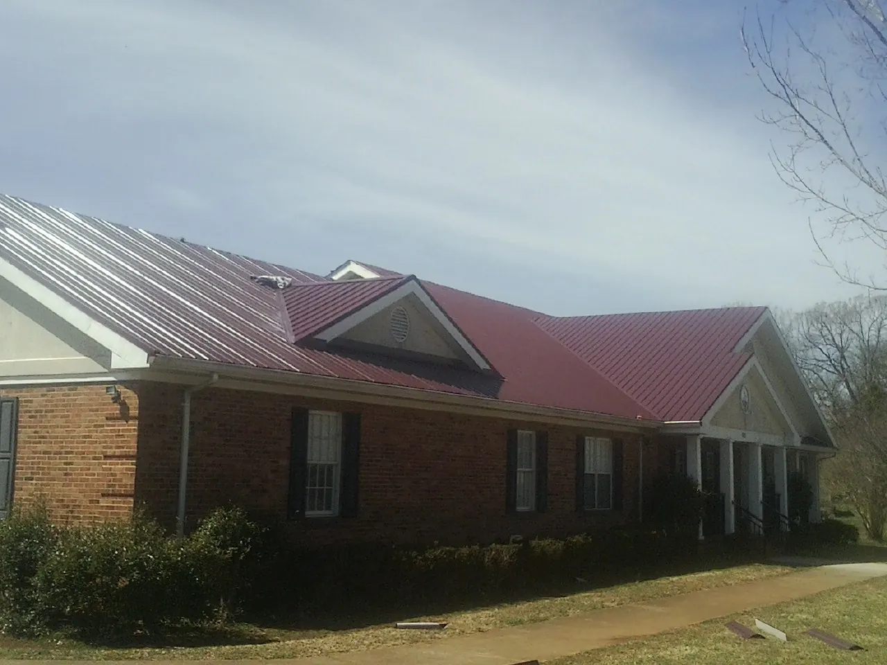 Red metal roof with gabled entries on a long brick building, from a Hail Damage Roof Repair job in Saegertown