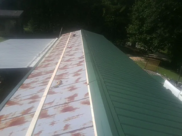 Old rusted panels beside newly installed green metal roofing — Wind Damage Roof Repair by Roofing Brothers in Saegertown