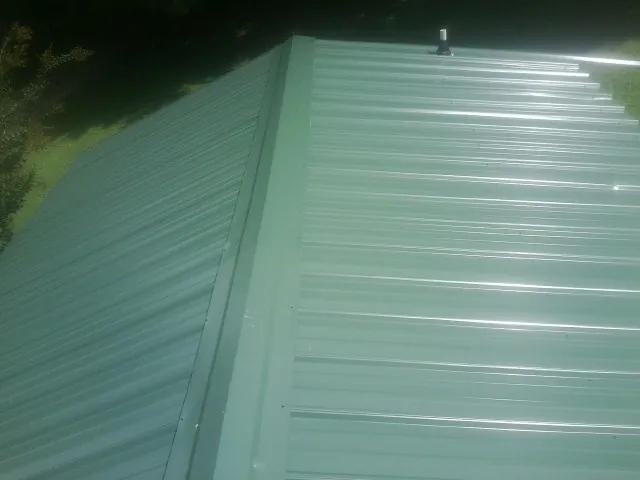 New green metal panels meeting at the ridge of a roof — Flat Roof Repair work by our crew in Saegertown