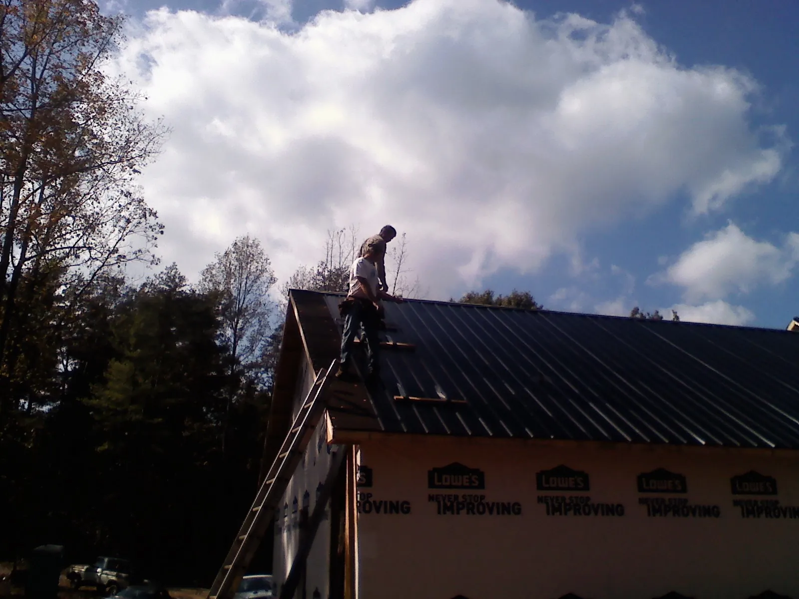 Roofer fastening dark metal panels high against a cloudy sky, from a Roof Inspection job in Saegertown