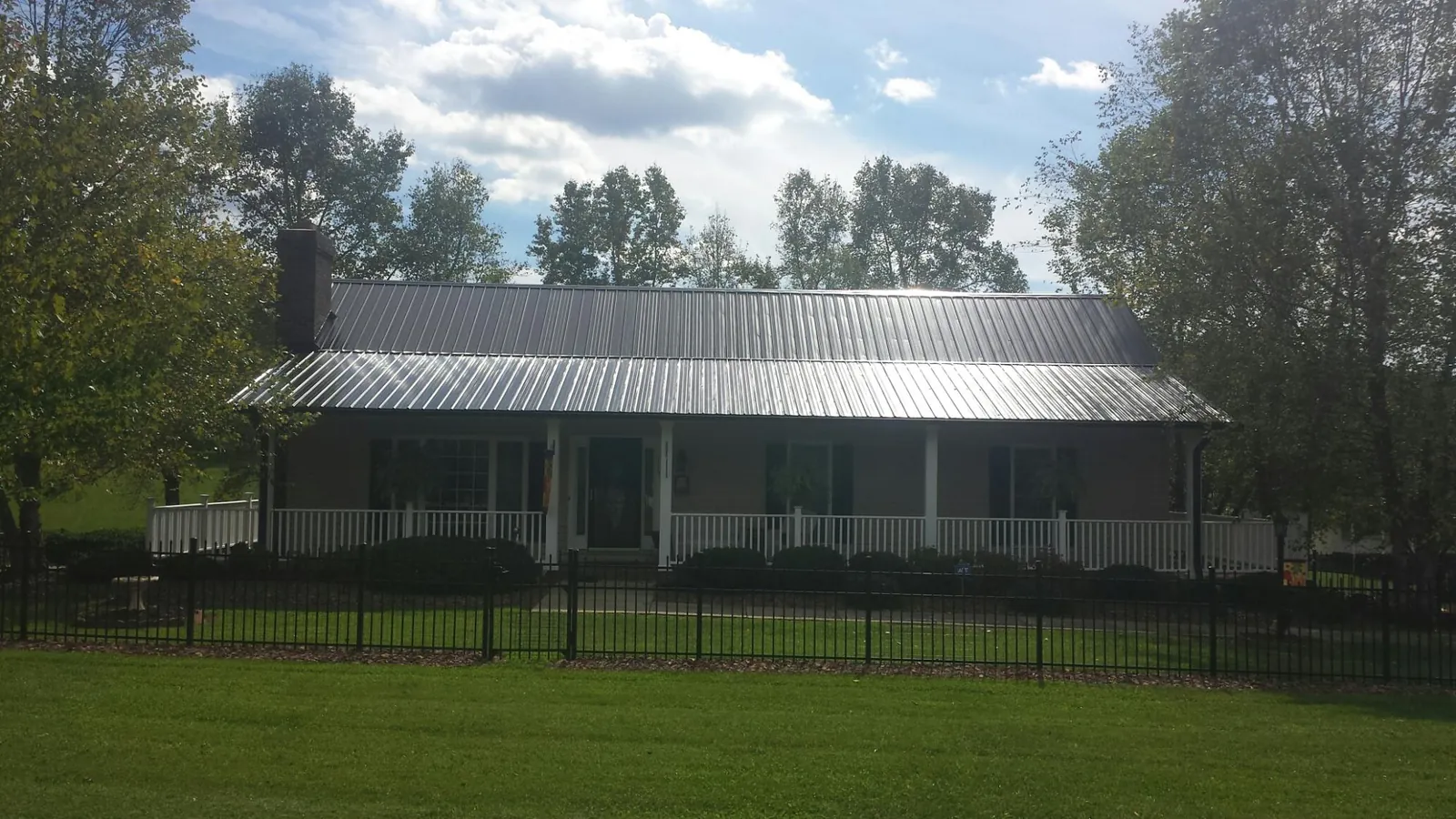 Gray metal roof on a brick ranch with a full width front porch — Gutter Guard Installation work by our crew in Saegertown