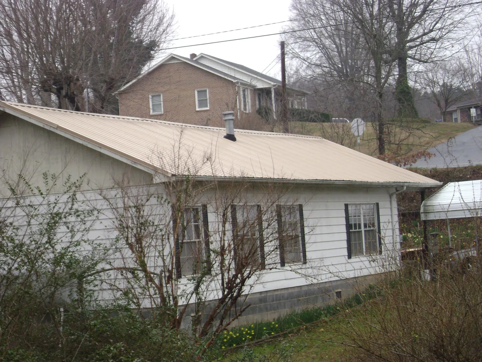 Tan metal roof on a white sided house set into a hillside — Commercial Roofing by Roofing Brothers in Saegertown