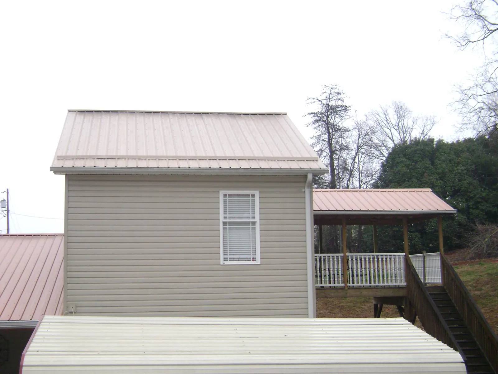 Tan metal roofs on a two story addition and attached porch, from a Roof Replacement job in Saegertown